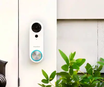 SimpliSafe Video Doorbell Pro installed on white siding beside a front door and garden plants