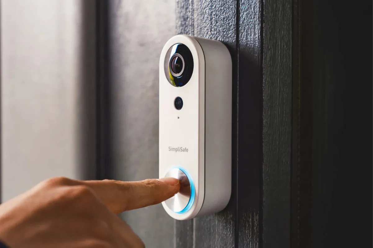 Visitor pressing the button on a SimpliSafe Video Doorbell Pro mounted beside a dark front door